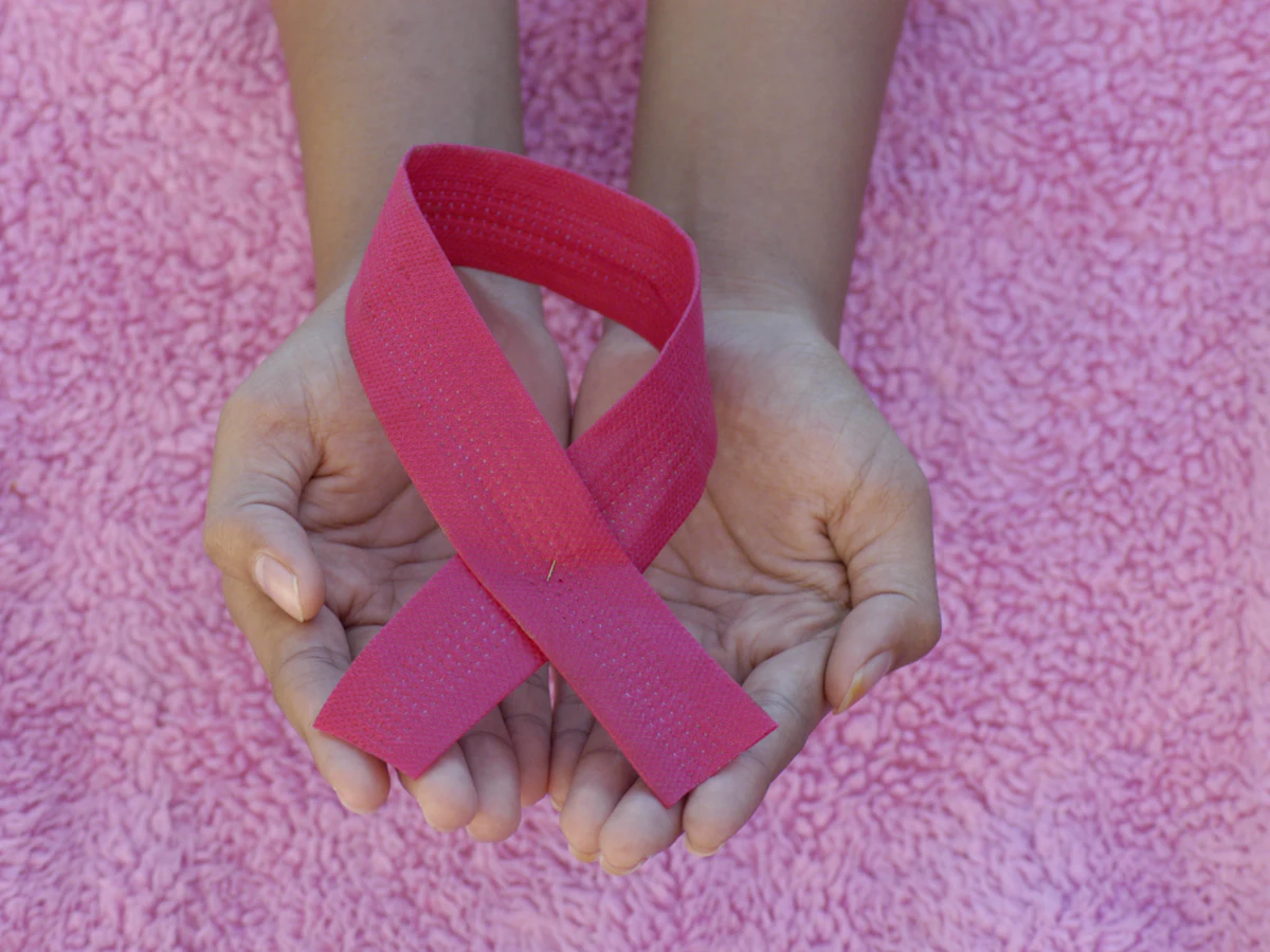 Deux mains réunies tiennent un ruban rose posé sur un tissu rose.