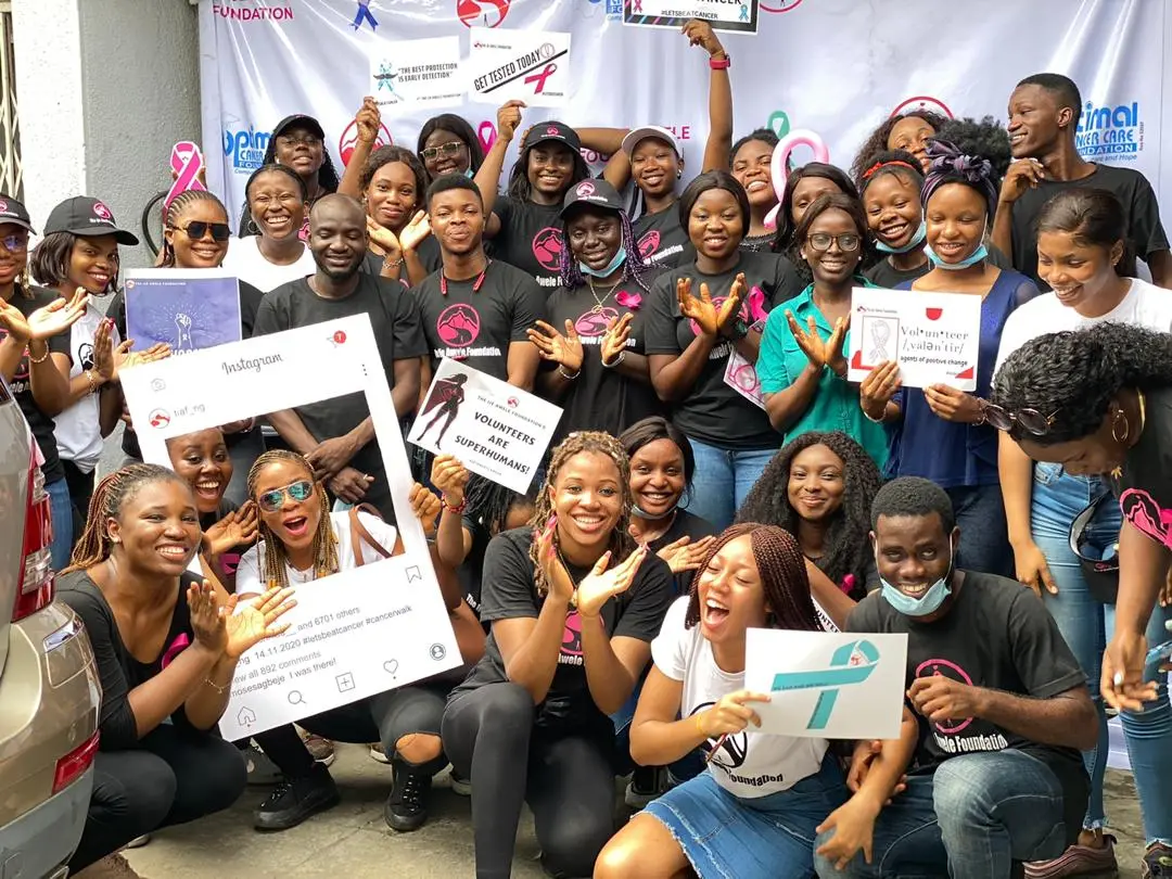 Un grand groupe de bénévoles souriants pose avec des pancartes de sensibilisation au cancer, dont « Get tested today ».
