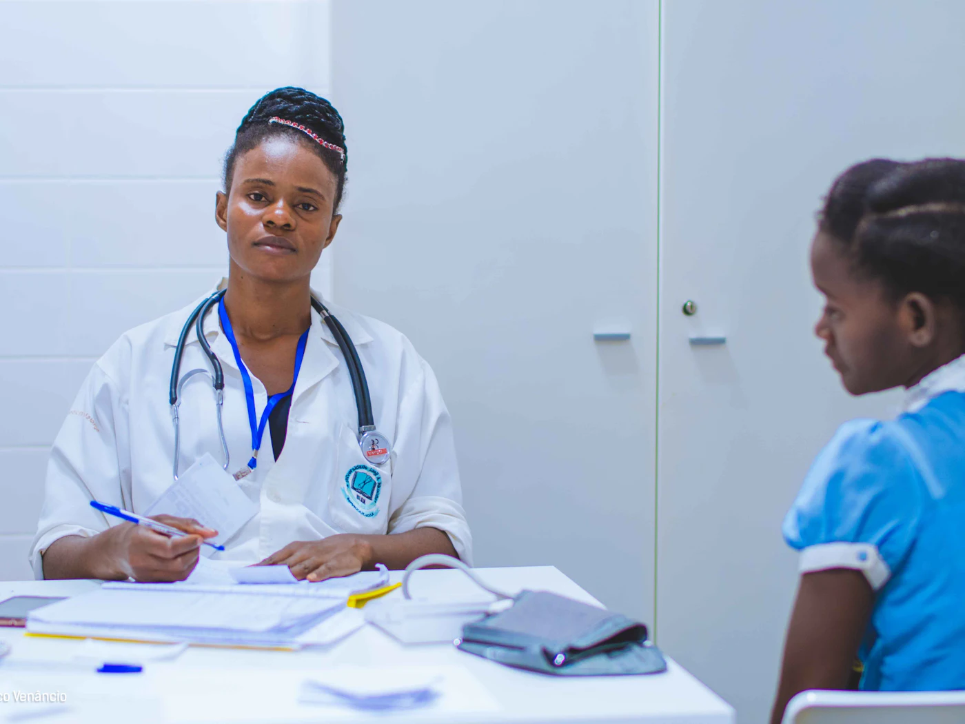 Une médecin en blouse blanche, stéthoscope autour du cou, échange avec une patiente dans un cabinet de consultation.