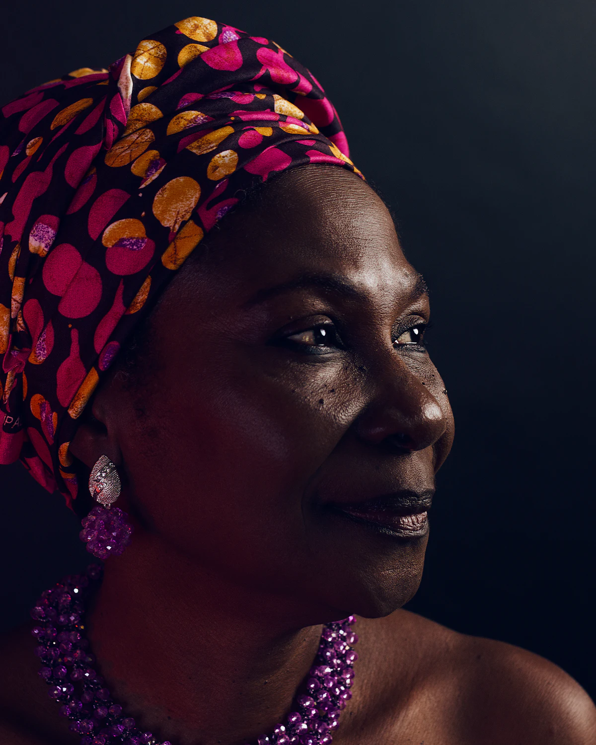Portrait d’une femme portant un foulard coloré, le regard tourné vers la lumière.
