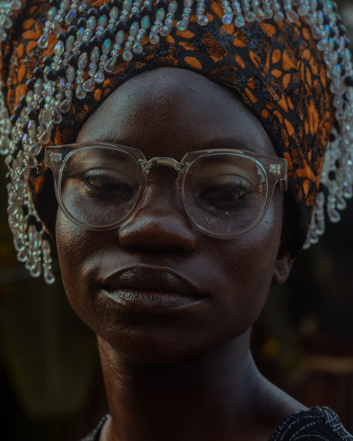 Portrait d’une femme aux lunettes transparentes, coiffée d’un foulard brodé de perles.