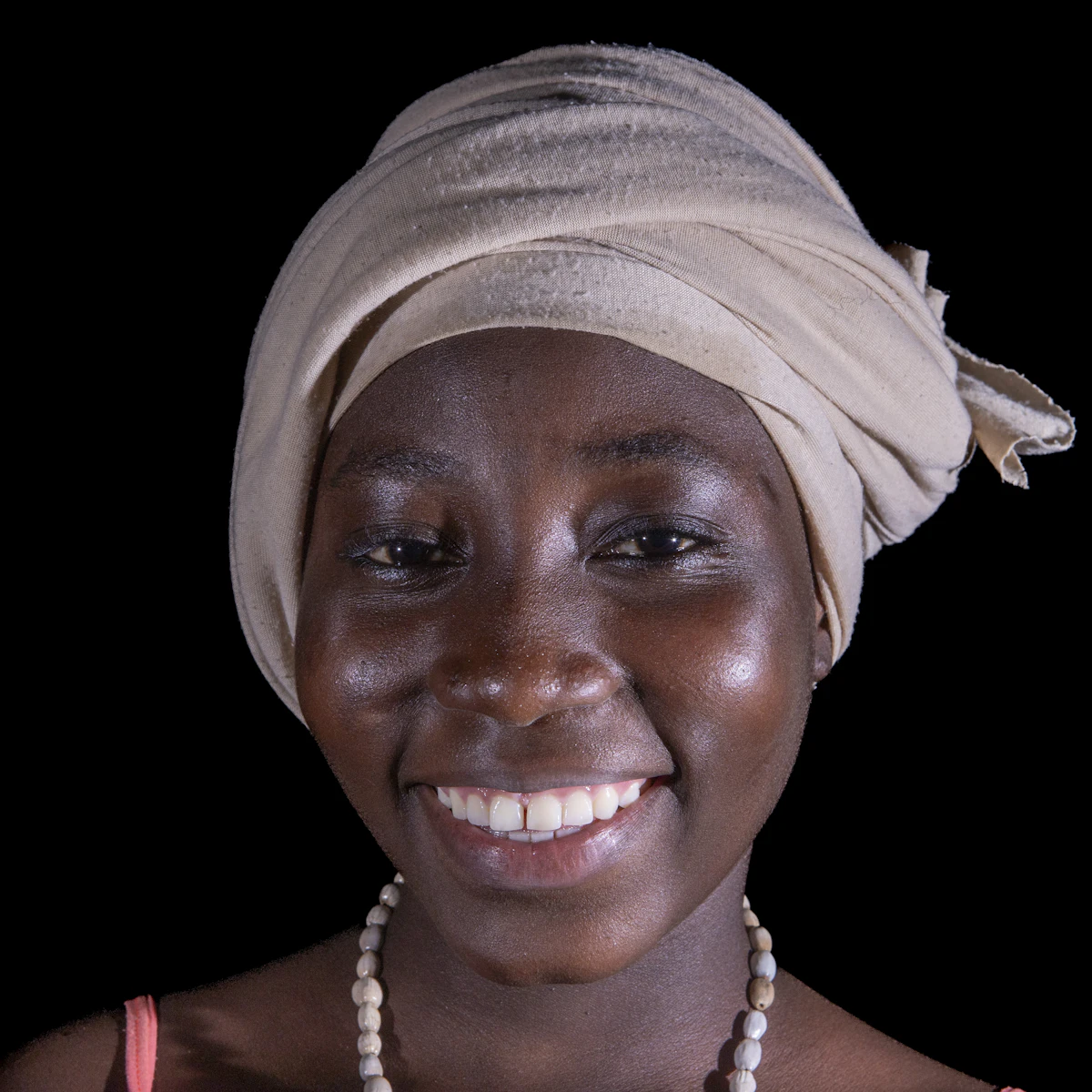 Portrait d’une femme souriante portant un foulard clair et un collier de perles.